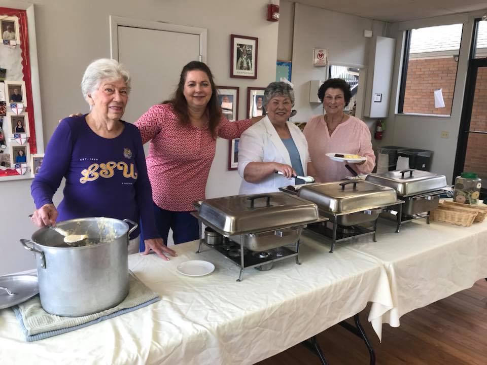 Women standing behind a long table, serving breakfast to other parishioners.